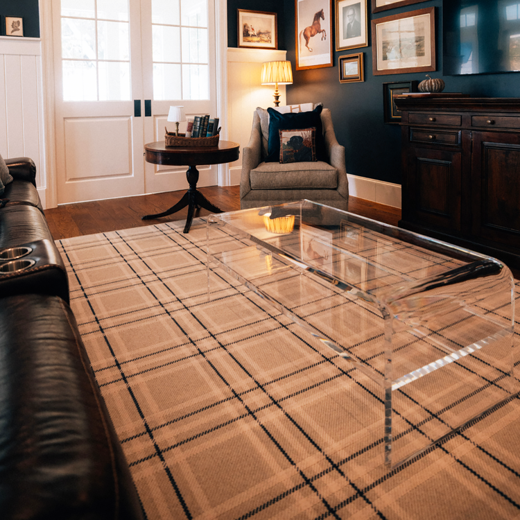 Living room with a leather couch, upholstered armchair, and a clear acrylic waterfall edge coffee table placed on a plaid rug.