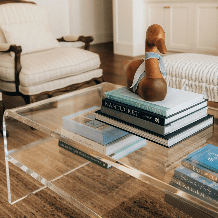 Clear acrylic coffee table with 1 interior shelf displaying books and decorative items in a living room setting.