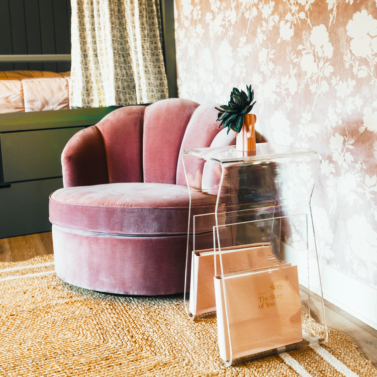 An acrylic lucite side table featuring legs that curve up into the inside of the table to double as a book or magazine rack sitting beside an easy chair.