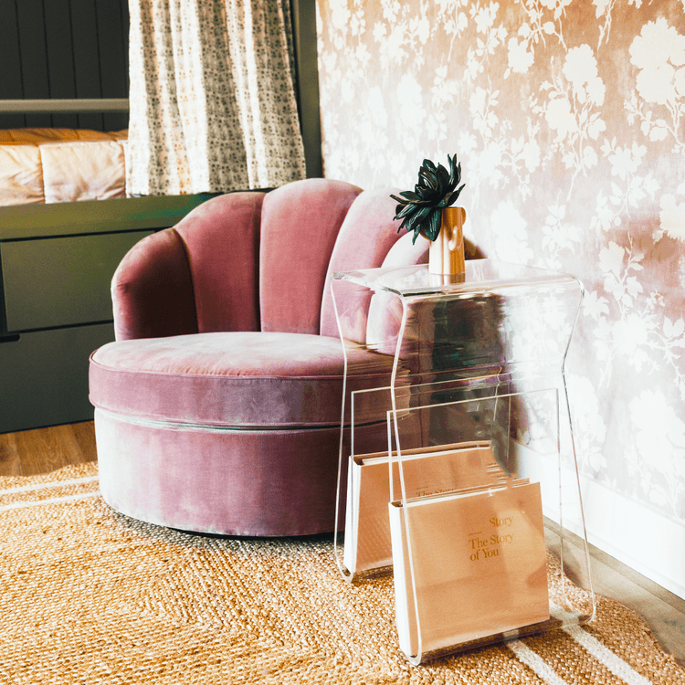 An acrylic lucite side table featuring legs that curve up into the inside of the table to double as a book or magazine rack sitting beside an easy chair.
