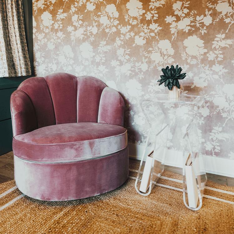 An acrylic lucite side table featuring legs that curve up into the inside of the table to double as a book or magazine rack sitting beside an easy chair.