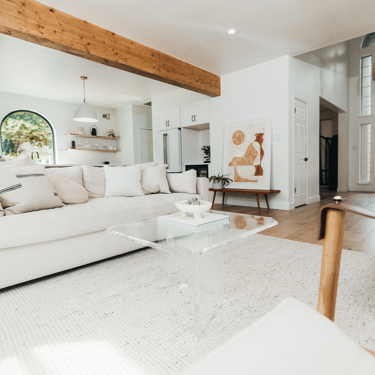 A clear acrylic lucite coffee table that features a thick u-shaped base displaying books and decor in a living room in front of a couch.
