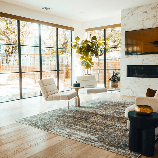 2 acrylic lucite lounge chairs with white cushions placed in a modern living room with many large windows. These chairs feature the white and off-white upholstery choices.