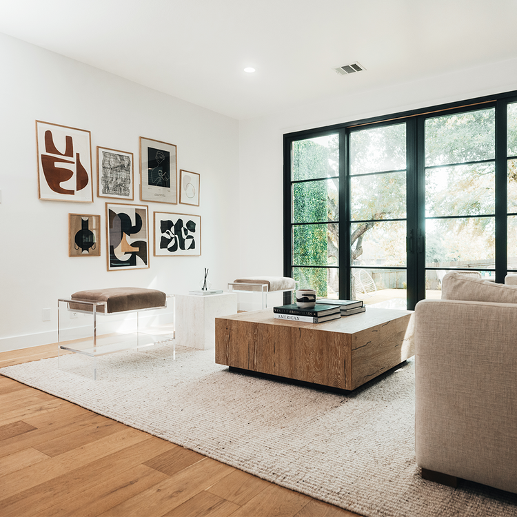Two clear acrylic benches with brown cushions and storage shelf underneath, placed as extra seating in a modern living room with abstract art on the walls.
