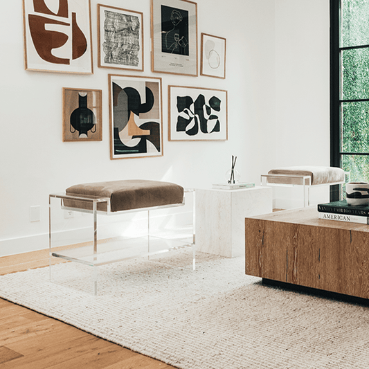 Two clear acrylic benches with brown cushions and storage shelf underneath, placed as extra seating in a modern living room with abstract art on the walls.