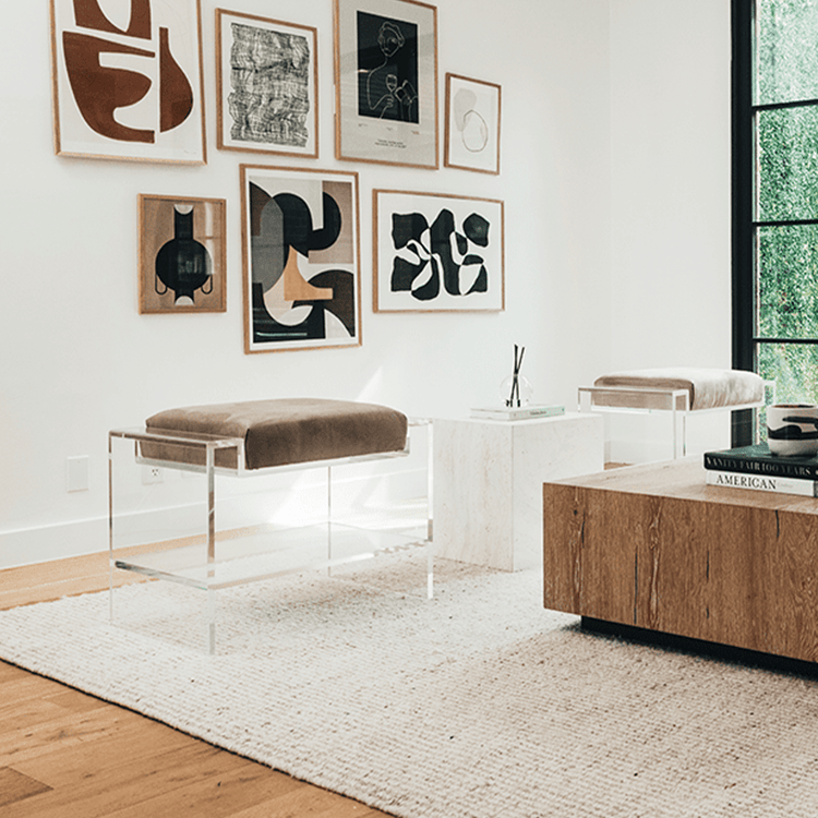 Two clear acrylic benches with brown cushions and storage shelf underneath, placed as extra seating in a modern living room with abstract art on the walls.