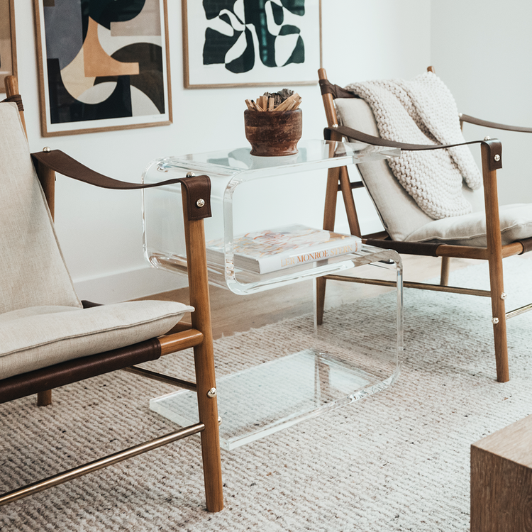 A clear acrylic side table shaped like the number 5 placed between 2 chairs in a living room.