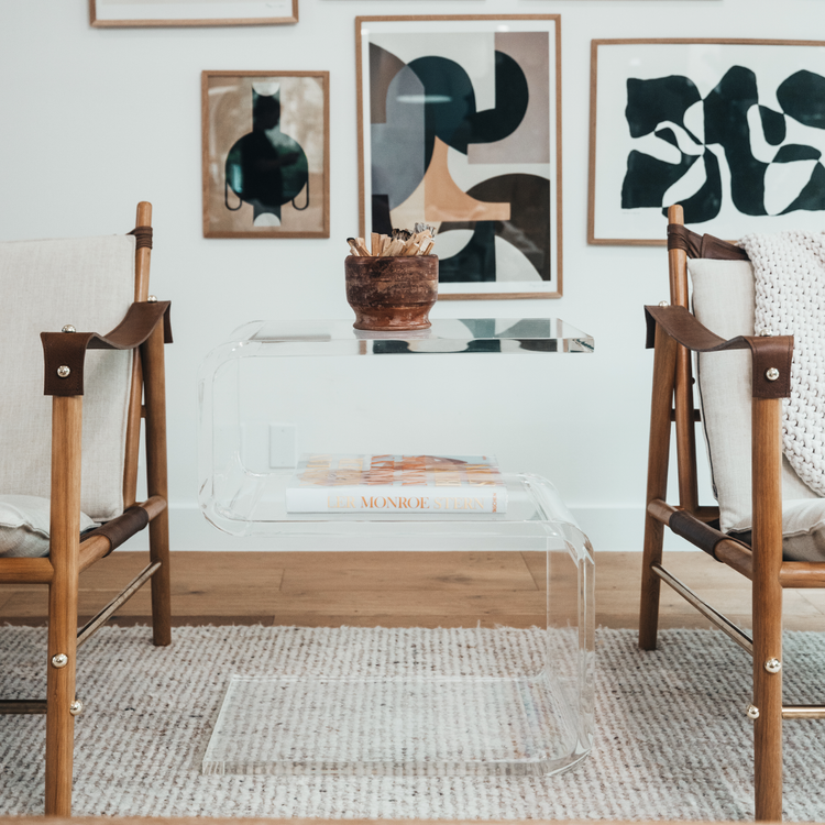 A clear acrylic side table shaped like the number 5 placed between 2 chairs in a living room.