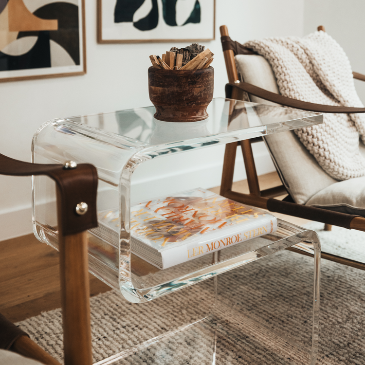 A clear acrylic side table shaped like the number 5 placed between 2 chairs in a living room.