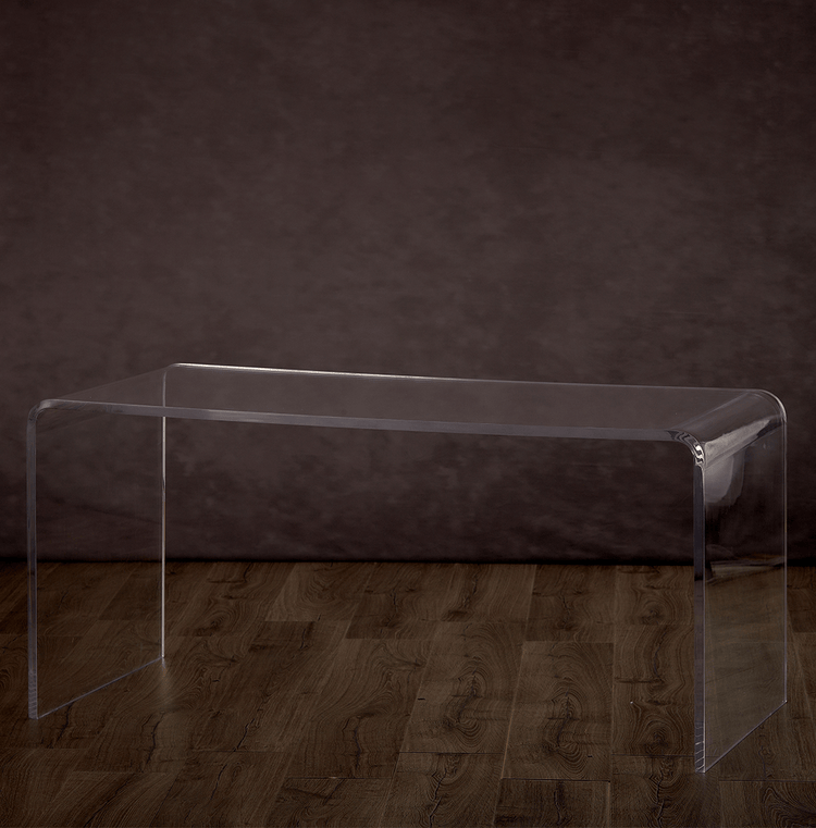 A clear acrylic vanity or desk against a dark wall with a hardwood floor.
