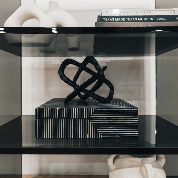 Closeup of a clear gray tinted acrylic lucite bookshelf with 3 interior shelves displaying books and decor placed against a living room wall.