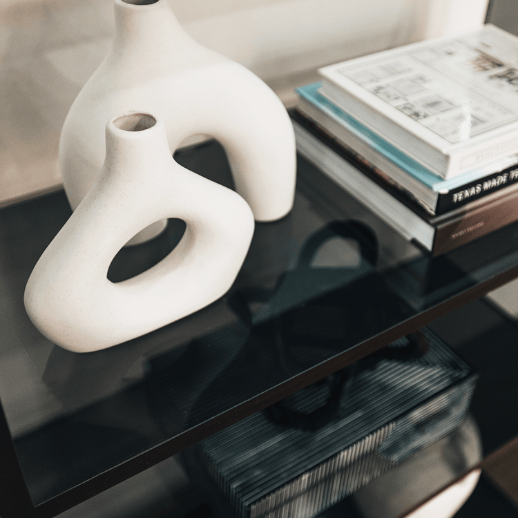 Closeup of 1 shelf of a clear gray tinted acrylic lucite bookshelf with 3 interior shelves displaying books and decor placed against a living room wall.