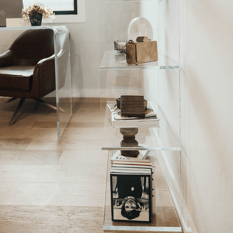 Sideview of a clear acrylic lucite bookshelf with 3 interior shelves displaying books, candle and decor.