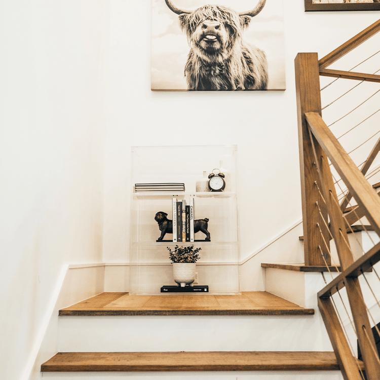 Clear acrylic lucite bookshelf with 3 interior shelves displaying books and decor placed on a stairway landing.