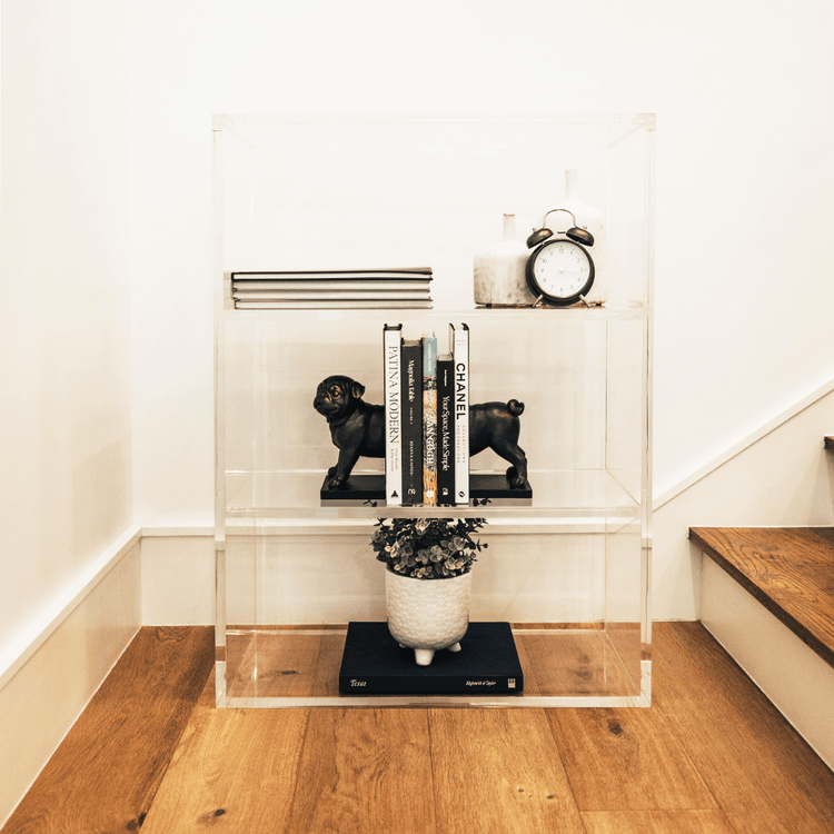 Clear acrylic lucite bookshelf with 3 interior shelves displaying books and decor placed on a stairway landing.