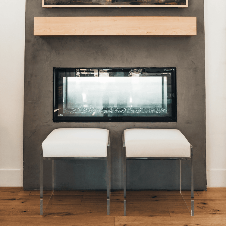 2 acrylic lucite upholstered accent chairs providing extra seating in front of a fireplace in a living room.