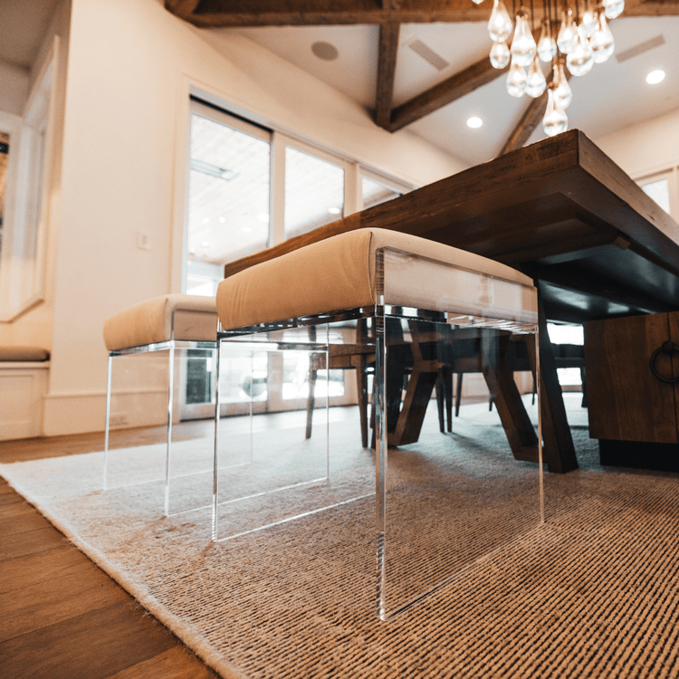 A closeup of 2 acrylic lucite upholstered accent chairs providing extra seating at the end of a dining room table.