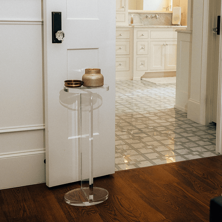 Clear acrylic side table with decorative items in a bathroom setting next to a door.