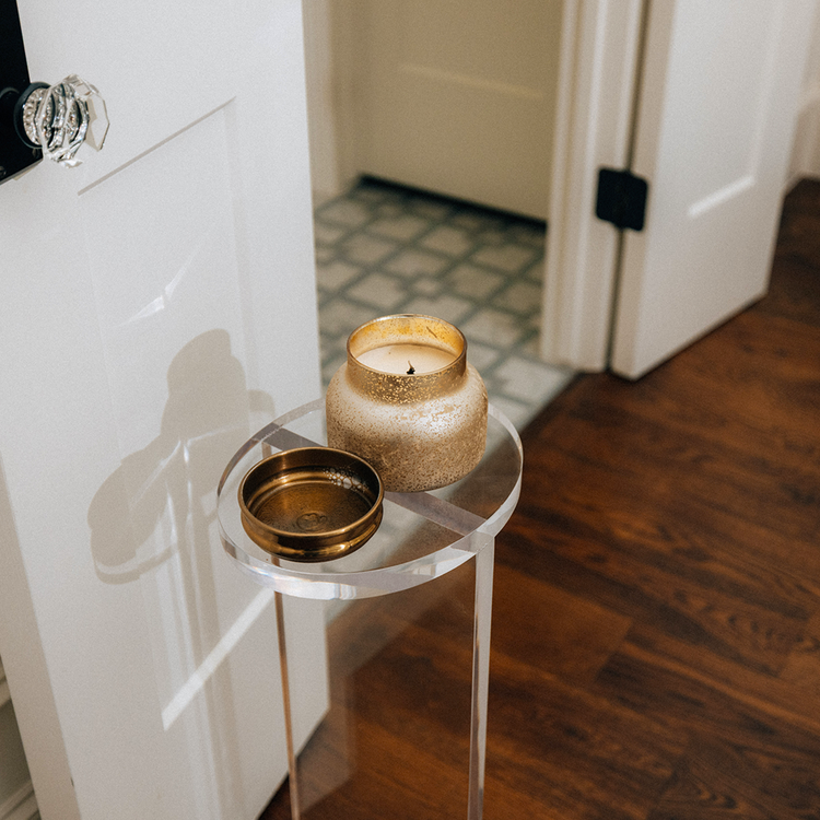 Clear acrylic side table with decorative items in a bathroom setting next to a door.