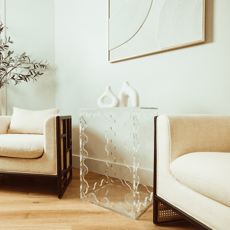 A clear acrylic lucite end table featuring wavy scalloped edges displaying ceramic decor placed between 2 easy chairs in a living room setting.