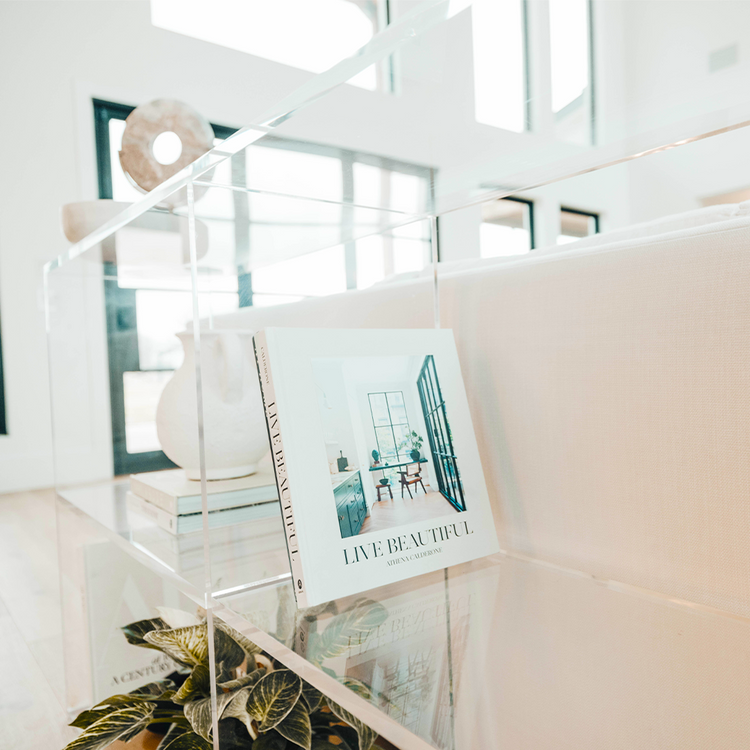 A closeup of the edges on a clear acrylic horizontal, 2 interior shelf bookcase displaying artwork, books, candles, and decor.