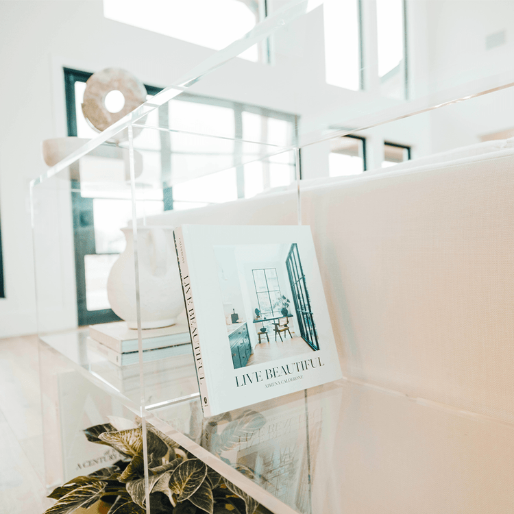 A closeup of the edges on a clear acrylic horizontal, 2 interior shelf bookcase displaying artwork, books, candles, and decor.