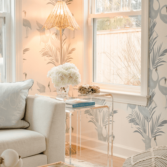 A clear acrylic nesting end table set placed in a living room setting beside a white sofa, with a lamp and decorative items on top.