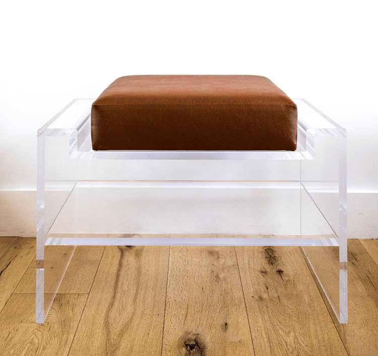 Catalog sample of a clear acrylic bench with a dark brown cushion and storage shelf underneath on a wooden floor.