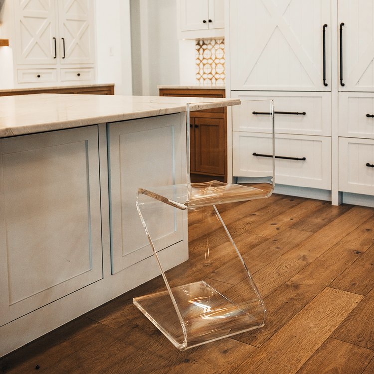 A clear acrylic bar stool with a modern design, placed in a kitchen setting next to a white countertop.