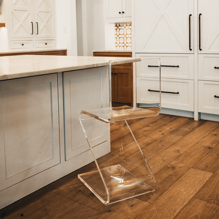 A clear acrylic bar stool with a modern design, placed in a kitchen setting next to a white countertop.