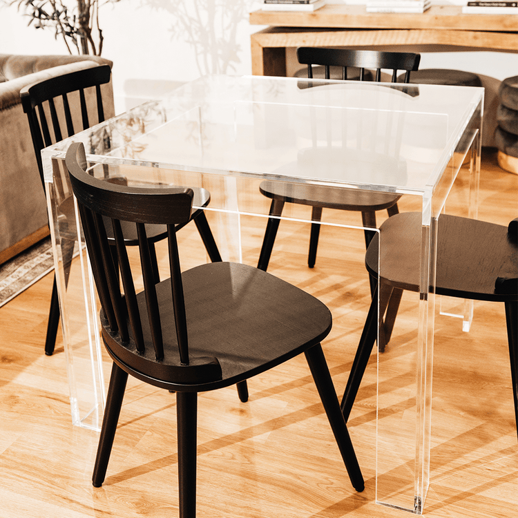 A closeup view of a square clear acrylic lucite game table featuring a chair on each side in a living room.