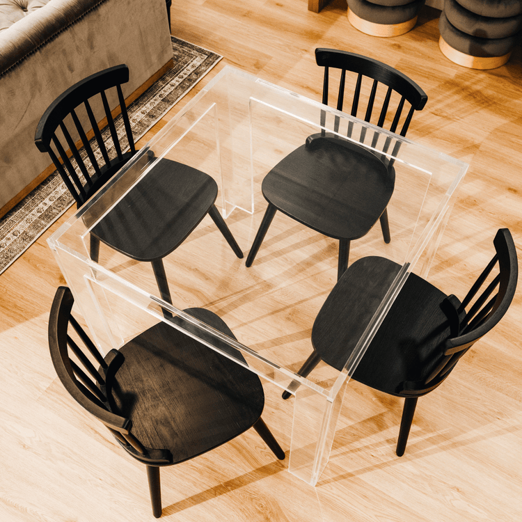 A top view of a square clear acrylic lucite game table featuring a chair on each side in a living room.