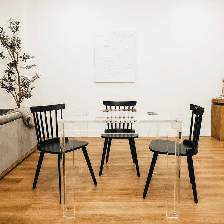 A side view of a square clear acrylic lucite game table featuring a deck of cards and a chair on each side of the table in a living room.
