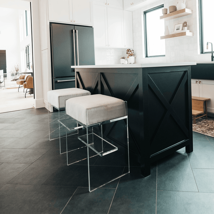 A set of two clear acrylic modern bar stools with white upholstered seats and clear acrylic legs, positioned at a kitchen island.