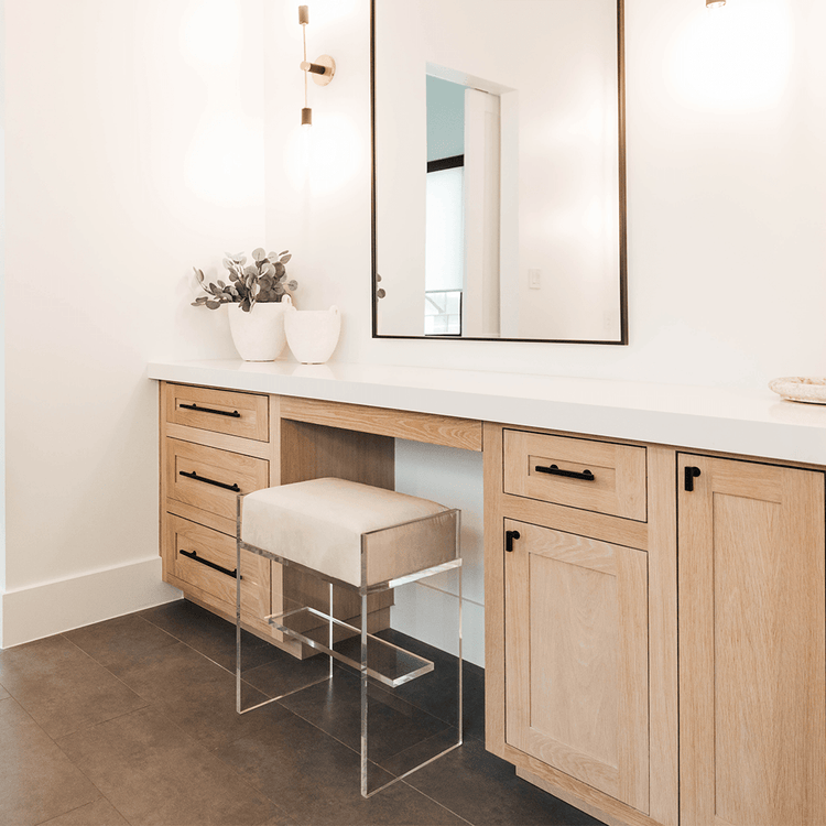 An acrylic bar stool with an off-white cushion used as a vanity seat at a bathroom counter.