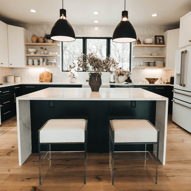 A set of two clear acrylic modern bar stools with white upholstered seats and clear acrylic legs, positioned at a kitchen island.