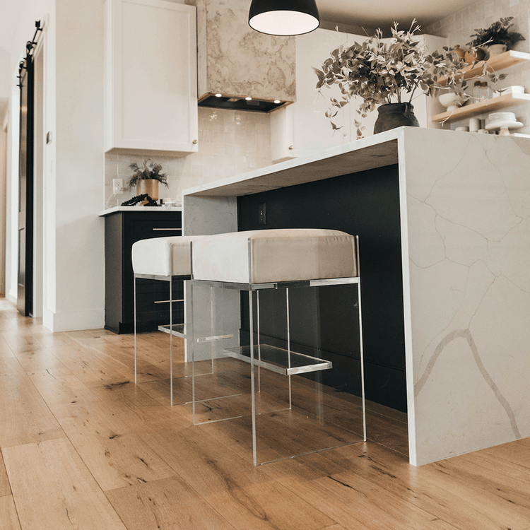 A set of two clear acrylic modern bar stools with white upholstered seats and clear acrylic legs, positioned at a kitchen island.