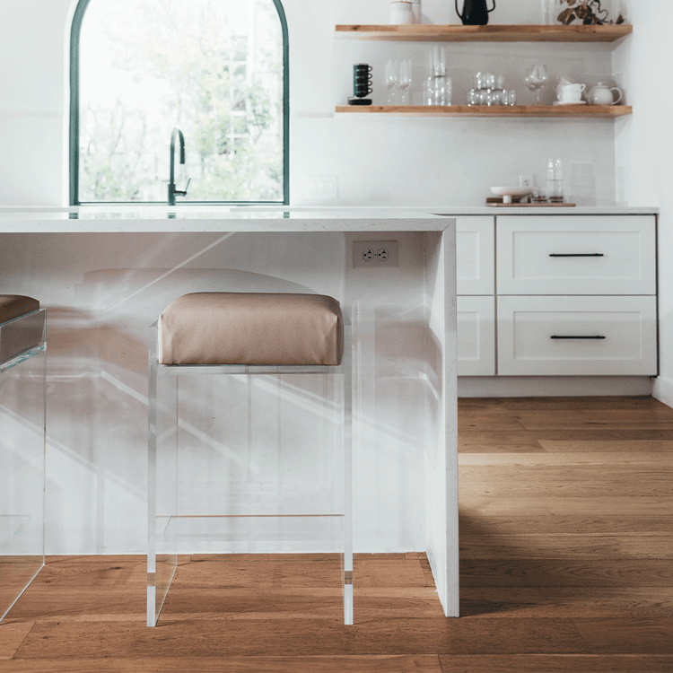 A set of two clear acrylic modern bar stools with beige upholstered seats and clear acrylic legs, positioned at a kitchen island.