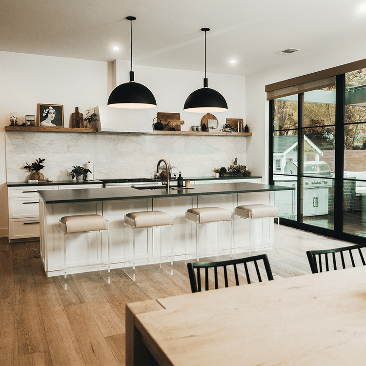 A set of four clear acrylic modern bar stools with beige upholstered seats and clear acrylic legs, positioned in a kitchen setting.