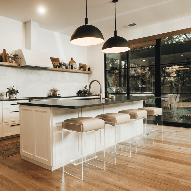 A set of four clear acrylic modern bar stools with beige upholstered seats and clear acrylic legs, positioned in a kitchen setting.