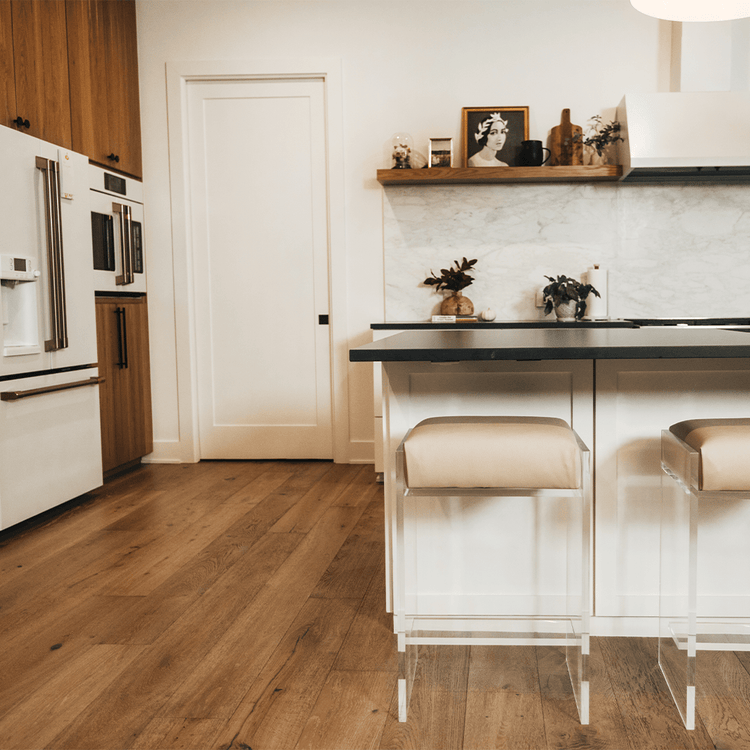 A close up of two stools out of a set of four clear acrylic modern bar stools with beige upholstered seats and clear acrylic legs, positioned in a kitchen setting.
