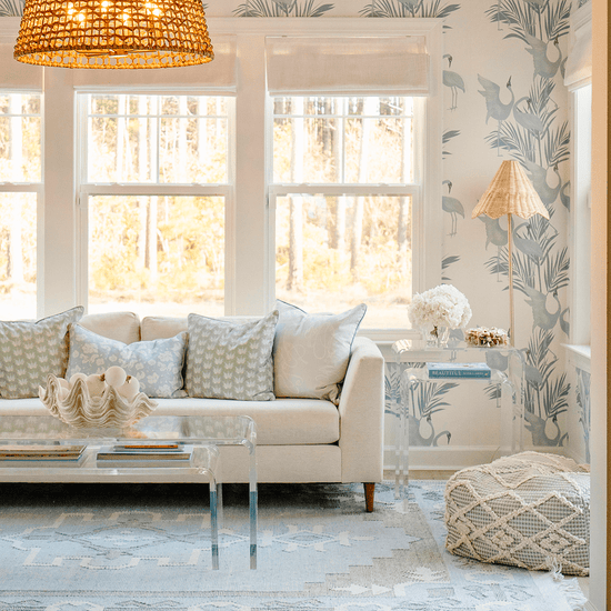 A clear acrylic lucite nesting coffee table set placed in a living room setting in front of a white sofa displaying decorative items on top and books on the smaller nesting table underneath. Also pictured to the side of the sofa is a clear acrylic lucite nesting side table set.