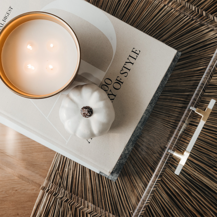 A clear acrylic lucite serving tray with gold and white handles holding decor, a candle, and books placed on a wooden table.