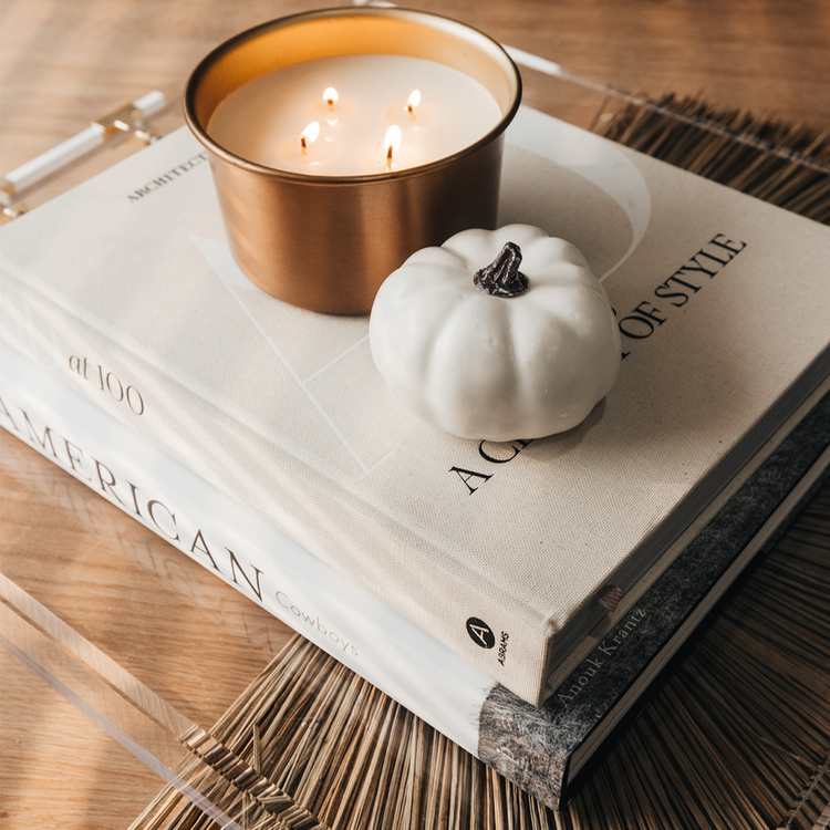 A clear acrylic lucite serving tray with gold and white handles holding decor, a candle, and books placed on a wooden table.