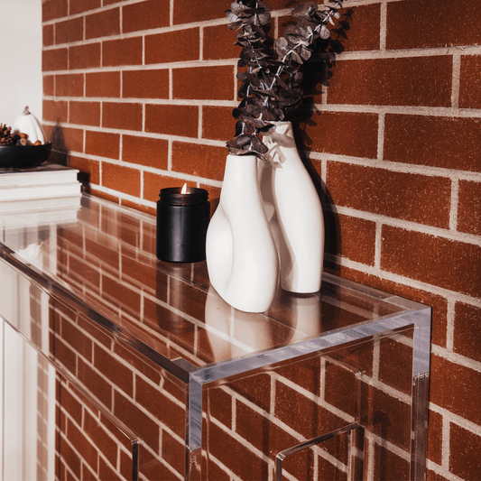 Clear acrylic slab entryway table in front of a brick wall displaying books, a candle, and decor.