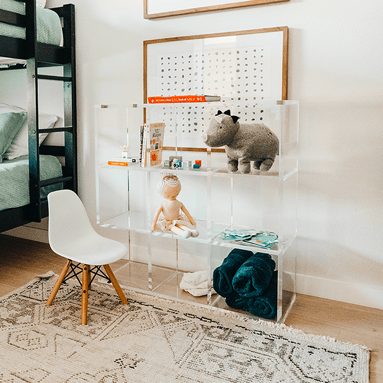 A clear acrylic lucite 9 cube storage unit displaying children's toys, blankets, and books in a child's bedroom. The unit features 3 rows of 3 cubes.