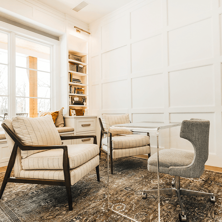 A clear acrylic waterfall edge desk placed in a modern office setting with a chair pushed underneath and 2 chairs facing it.
