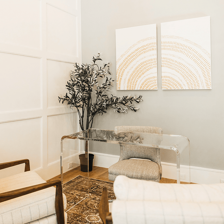 A clear acrylic waterfall edge desk placed in a modern office setting with a chair pushed underneath and 2 chairs facing it.
