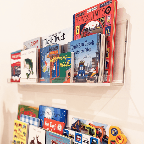 A set of clear acrylic floating bookshelves mounted on a wall, displaying various children's books.
