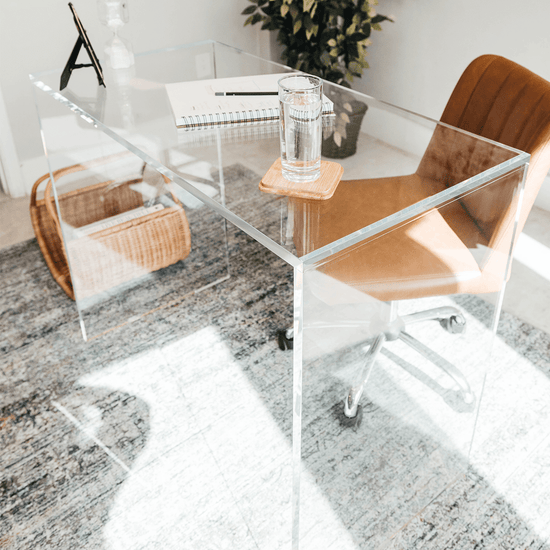 An acrylic lucite slab desk with a brown leather chair in front, placed in an office setting.